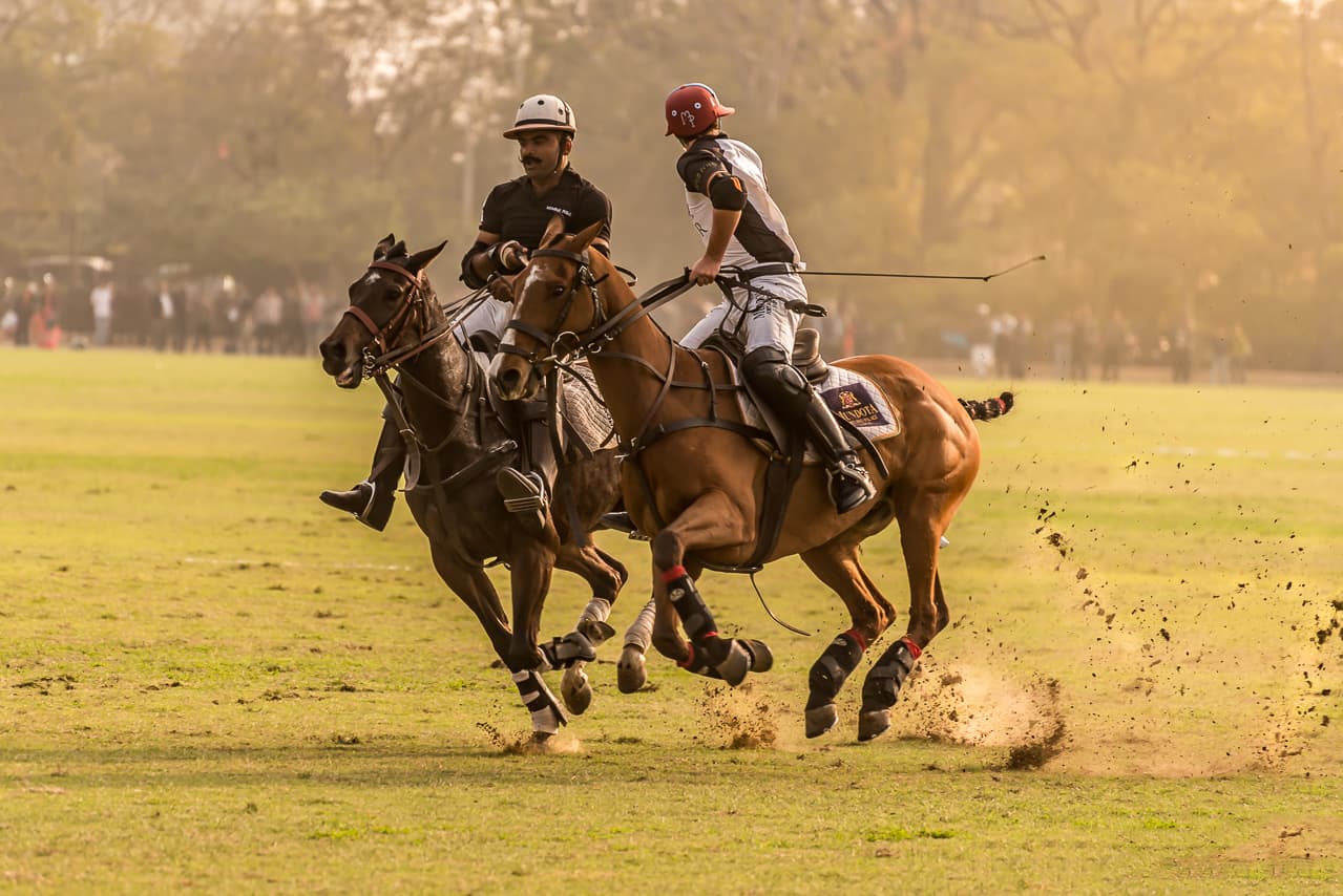 Two polo riders crossing in a burst of dust